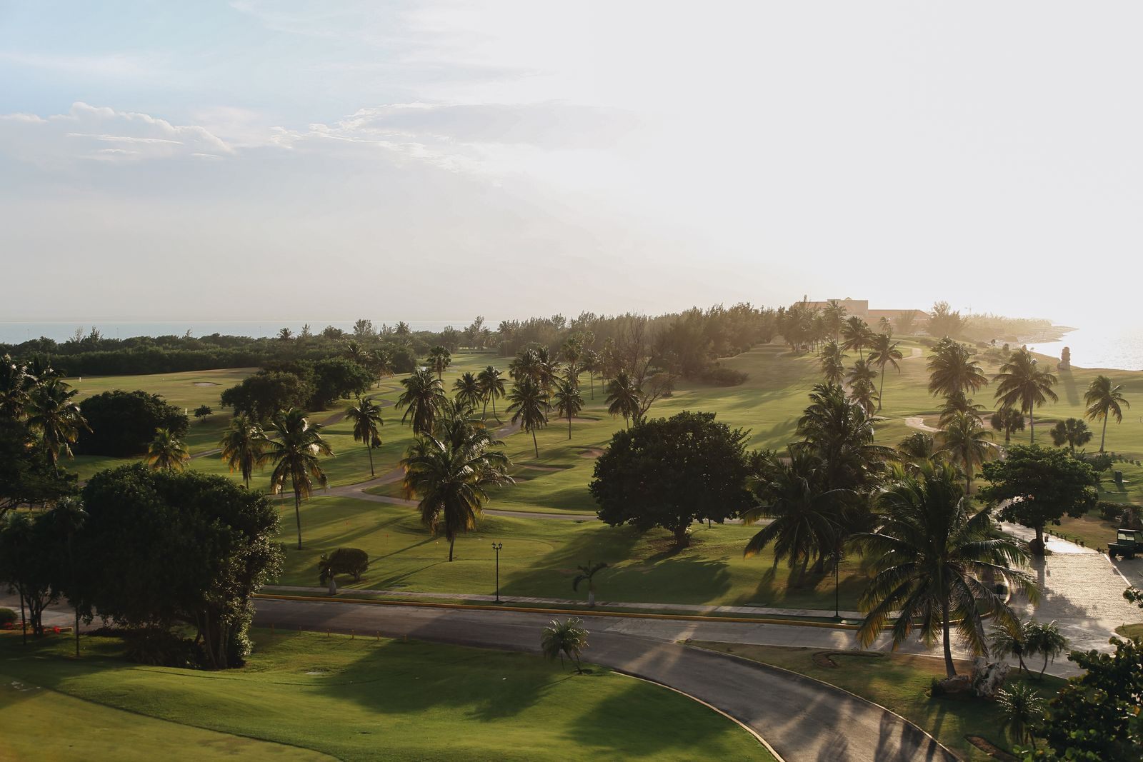 Aerial view of a tropical golf course with palm trees and the sea at sunrise