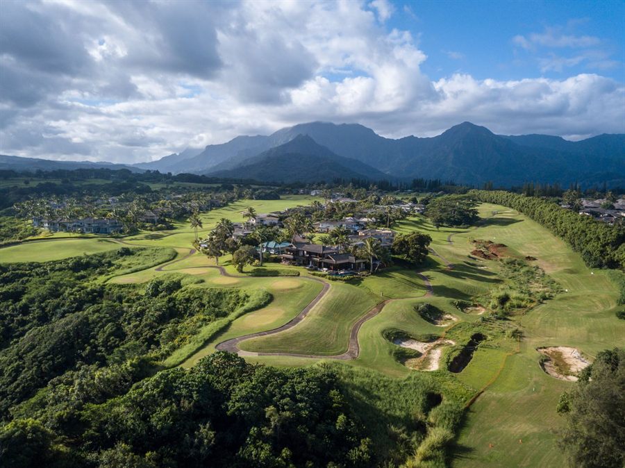 Aerial view of a tropical golf course in a green valley below jagged mountains